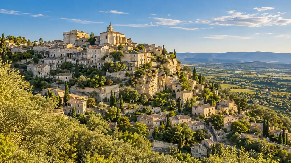 Travel to France: How to Plan a First Trip Beyond Paris 2 The stone village of Gordes rises above green countryside in Provence under warm afternoon light.
