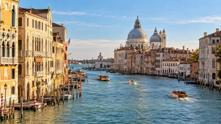 Home 8 Boats cross Venice’s Grand Canal beneath the domes of Santa Maria della Salute in warm afternoon light.