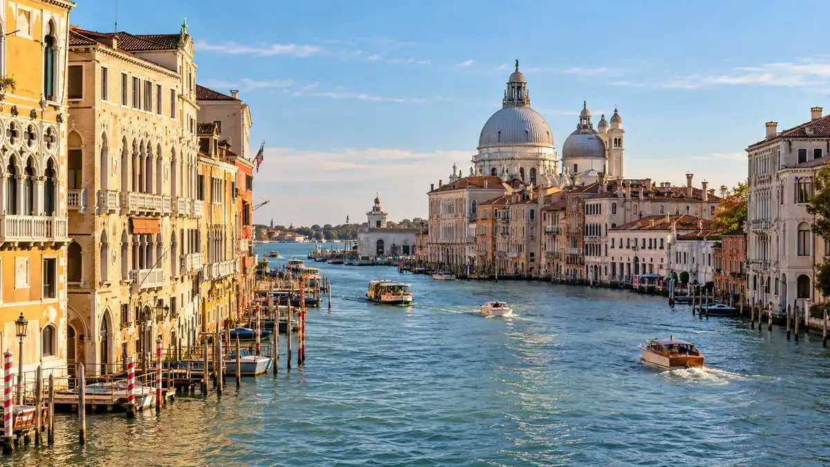 Travel to Italy: How to Plan Your First Trip 2 Boats cross Venice’s Grand Canal beneath the domes of Santa Maria della Salute in warm afternoon light.