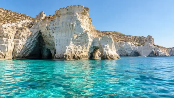 Milos 3 Day Itinerary: One Coast a Day, Kleftiko by Boat 11 White coastal rocks with sea caves and a natural opening rise above turquoise water at Kleftiko, Milos, with a distant sailboat.