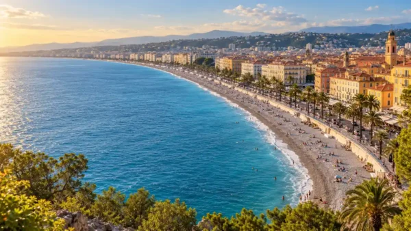 Travel to Nice, France: How to Plan Your First Trip 9 AI-generated view of Nice’s curved pebble beach, blue Mediterranean water and seafront promenade in warm afternoon light.