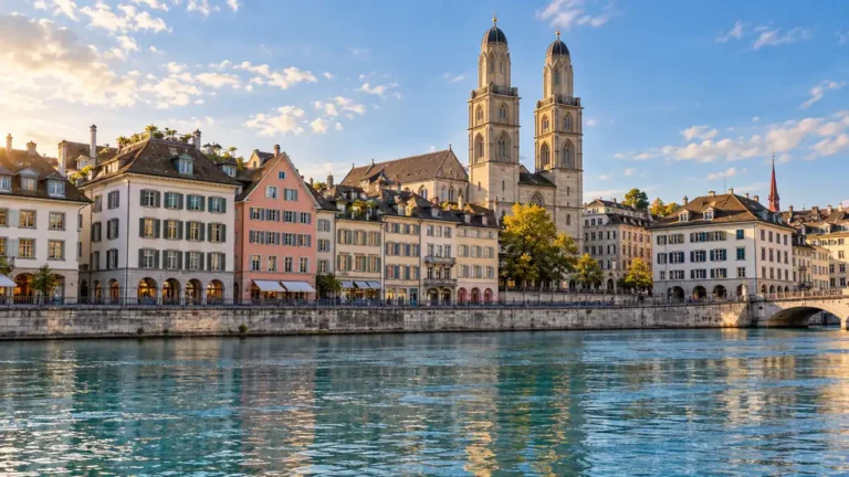 Home 34 AI-generated view of Zurich’s Limmat waterfront, historic facades and the twin towers of the Grossmünster in warm light.